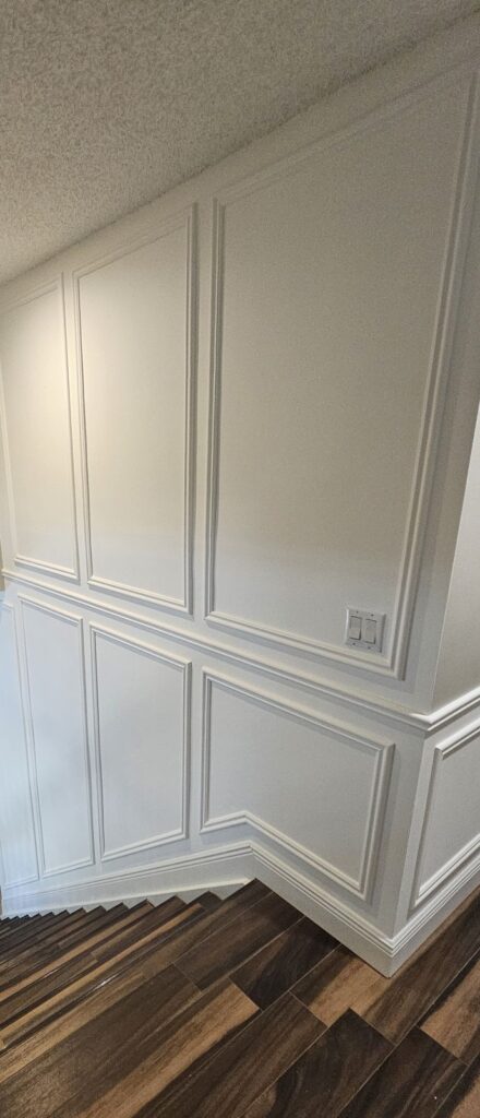 Two-tier white picture-frame wainscot at a hallway corner over dark wood floors