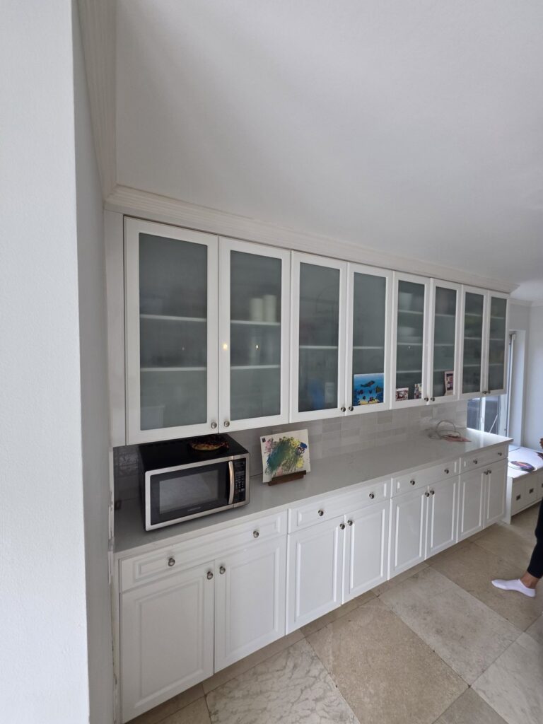 Built-in white kitchen cabinets with glass-front uppers and a microwave nook