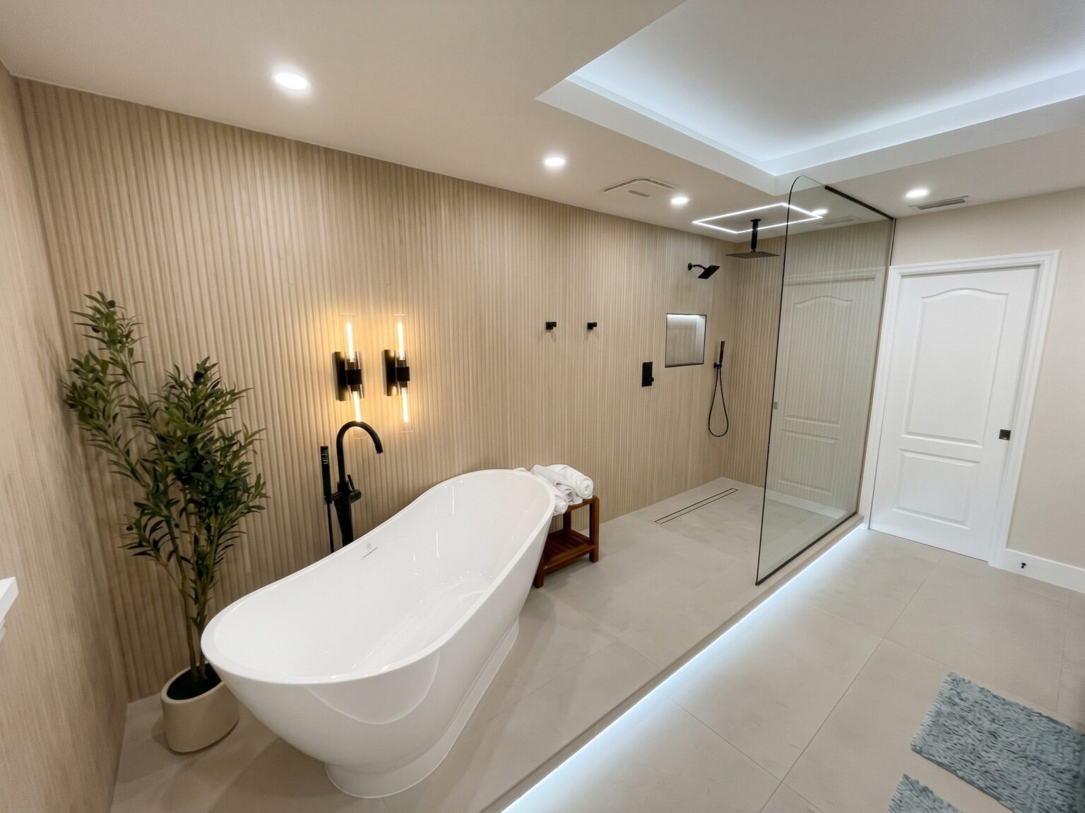 Remodeled master bathroom with a freestanding tub, wood-look slat wall, black sconces and LED ceiling cove