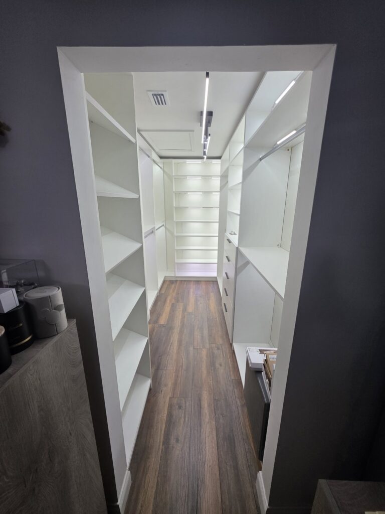 Walk-in closet with white built-in shelving and wood-look floors