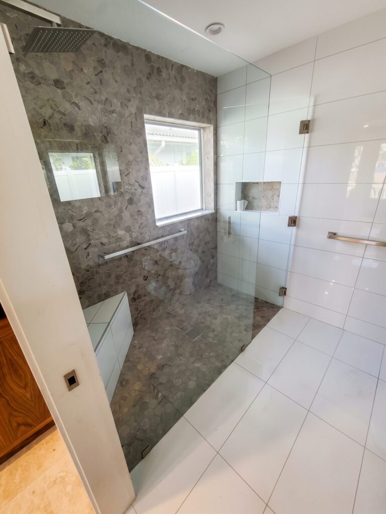 Finished walk-in shower with frameless glass, stone-look wall, niche and grab bar