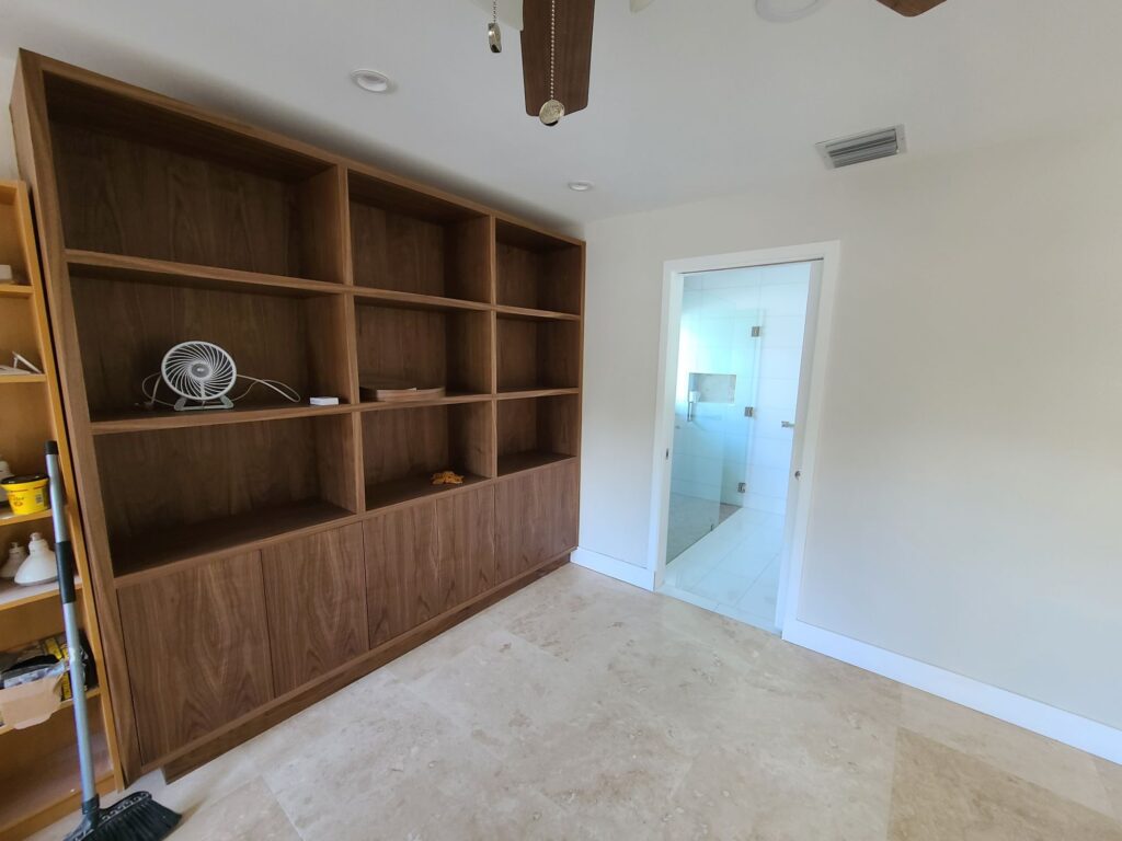 Full-wall walnut built-in bookshelf over a travertine floor