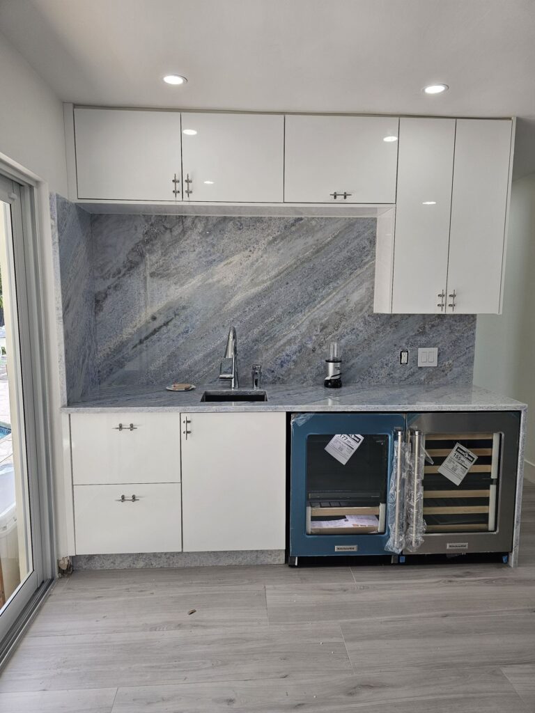 Wet bar with gloss white cabinets, a full-height marble slab backsplash and a wine fridge