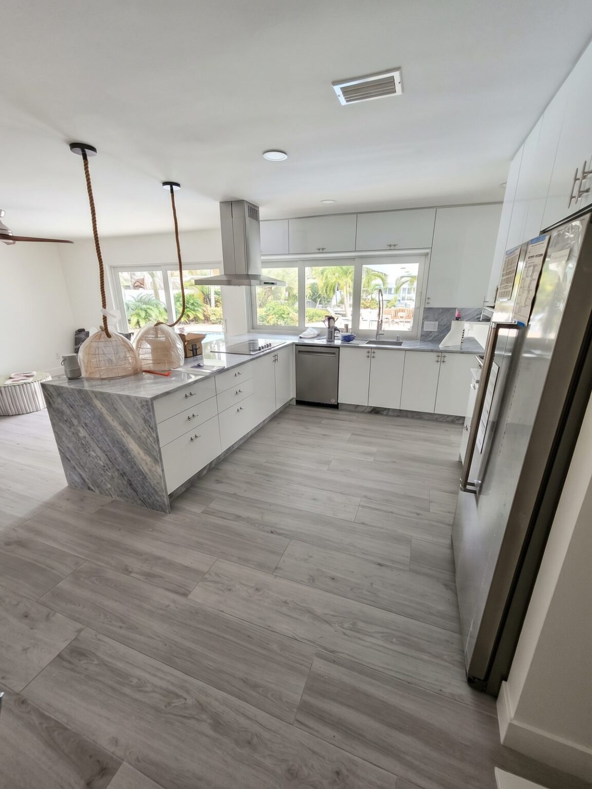 Finished white and gray kitchen with a waterfall island, pendant lights and gray plank floor