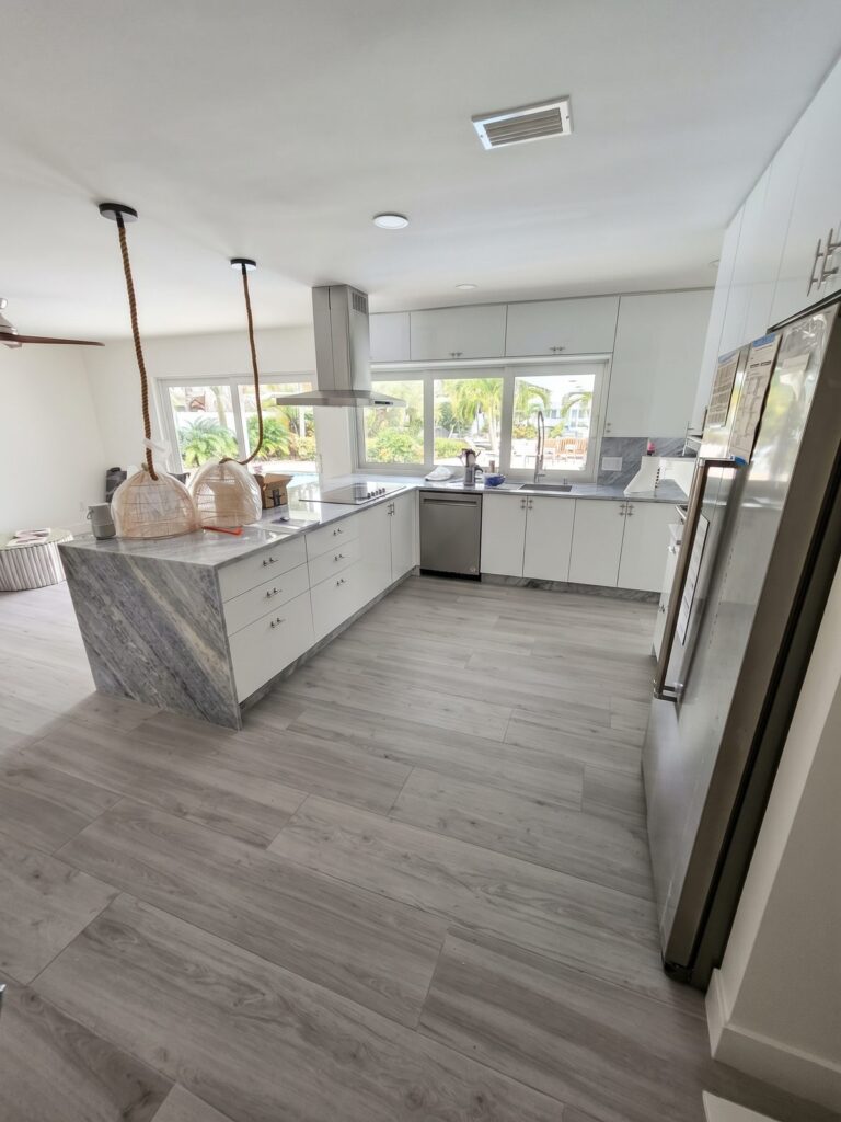Finished white and gray kitchen with a waterfall island, pendant lights and gray plank floor