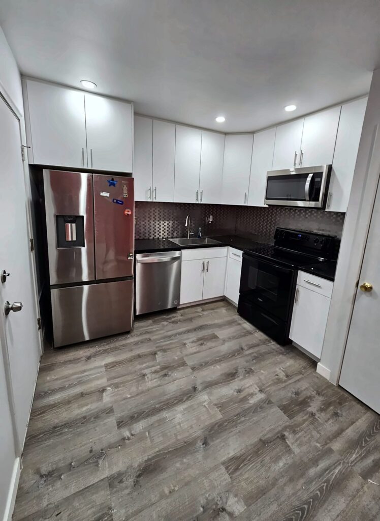 Same kitchen after the remodel with new white cabinets, dark counters, mosaic backsplash and new floor