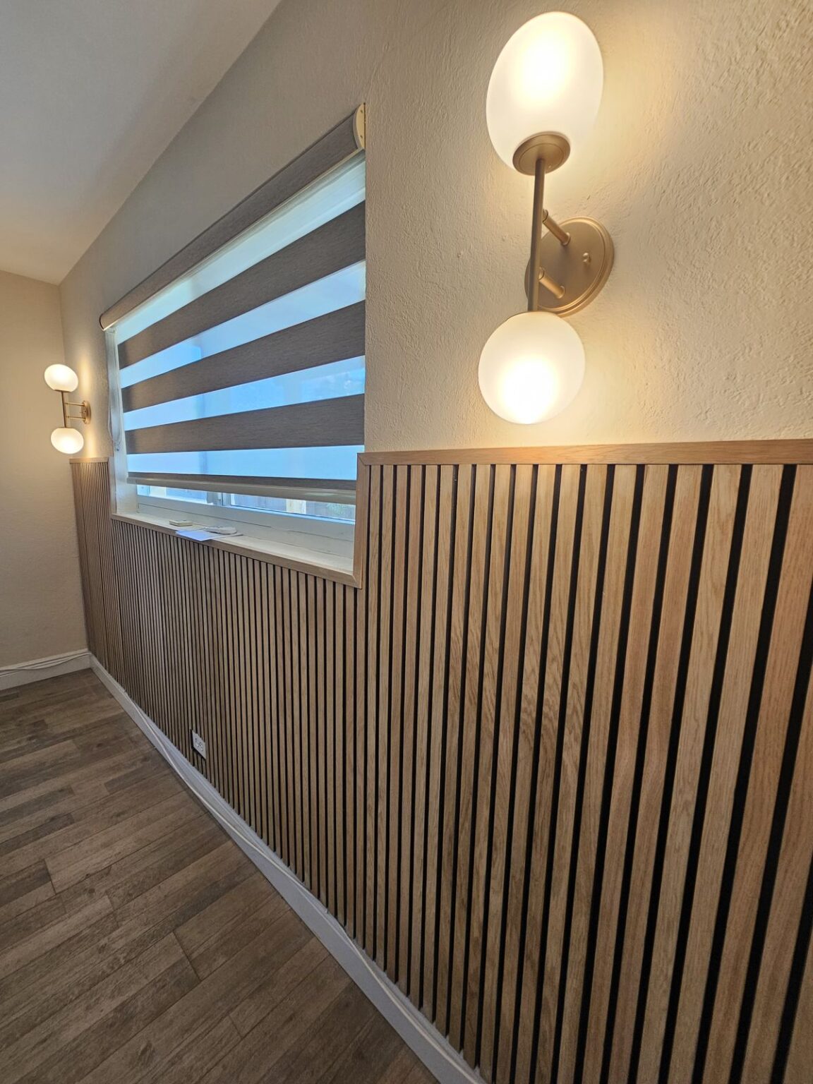 Light oak wood slat wainscot with globe wall sconces, finished bedroom accent wall in Palm Beach County